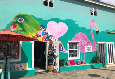 Afbeelding van de 'Beach Vibes' winkel in Bonaire, met trendy kleding en surfkleding, aangevuld met een levendige muurschildering.