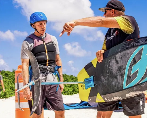 Persoon die leert kitefoilen op het water van Bonaire met een instructeur die de details van de foil uitlegt. Duik in kitefoillessen of huur materiaal bij onze partner en geniet van speciale kortingen op pick-up verhuur bij Pickup Huren Bonaire.